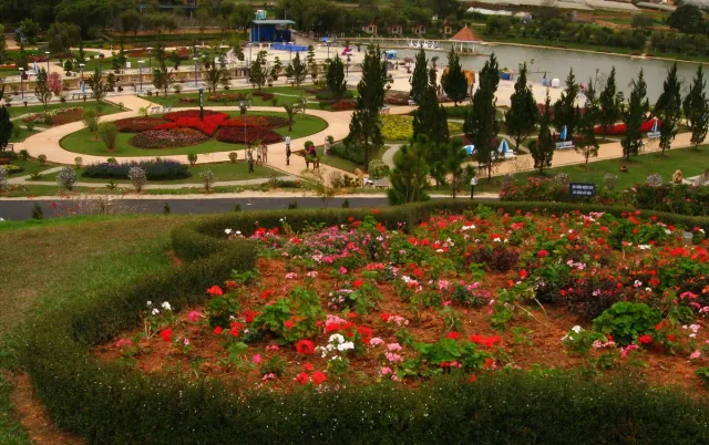 ערוגות פרחים אדומים וירוקים בגן מטופח עם עצים ברקע